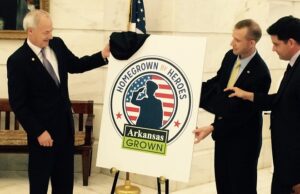 Gov. Asa Hutchinson joins Arkansas Agriculture Secretary Wes Ward (center) and Arkansas Veterans Affairs Director Matt Snead to unveil the logo for the new Homegrown by Heroes Arkansas Grown program in the state Capitol rotunda.