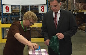 Arkansas Foodbank CEO Rhonda Sanders and U.S. Sen. John Boozman fill bags with food for the Food For Kids program. Behind them is the new logo for the organization.