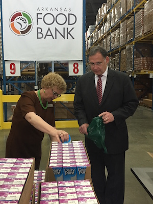 Arkansas Foodbank CEO Rhonda Sanders and U.S. Sen. John Boozman fill bags with food for the Food For Kids program. Behind them is the new logo for the organization.