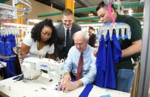 Gov. Asa Hutchinson tries his hand at sewing with a group of employees at TY Garments at their new textile and apparel facility in Little Rock.