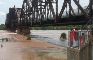 The Arkansas River rises against the Rock Island Bridge near the Clinton Presidential Center on June 2 as people watch from the north bank.