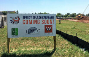 A sign at a construction site promotes a new Speedy Splash Car Wash location.