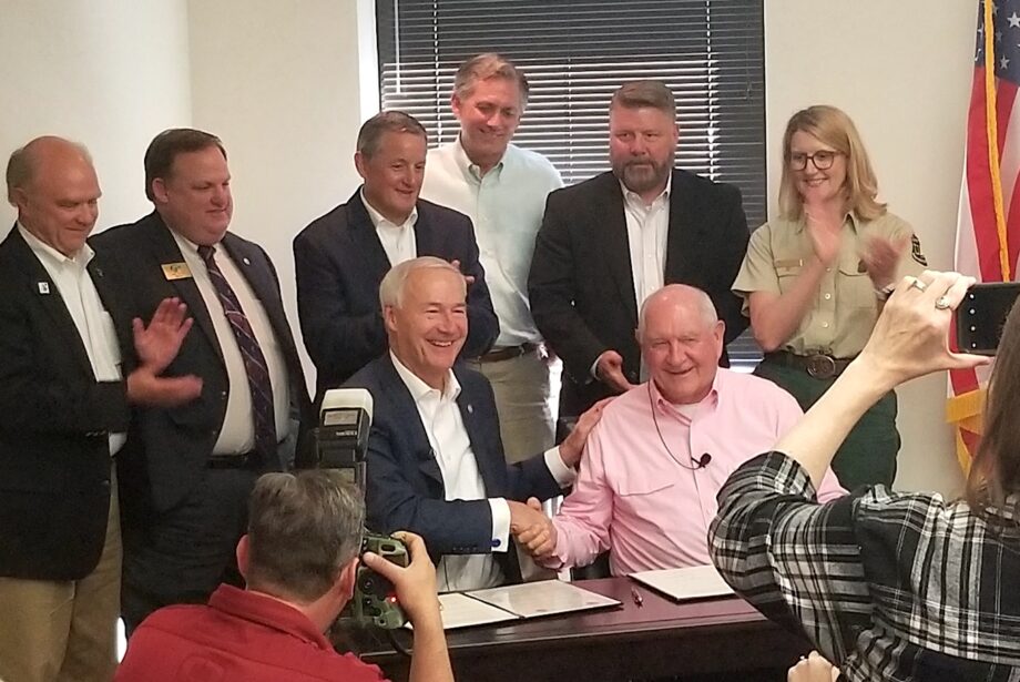 Gov. Asa Hutchinson and U.S. Secretary of Agriculture Sonny Perdue (seated) shake hands and pose for photographs in Little Rock. U.S. Reps. Bruce Westerman, French Hill, Rick Crawford and others look on.