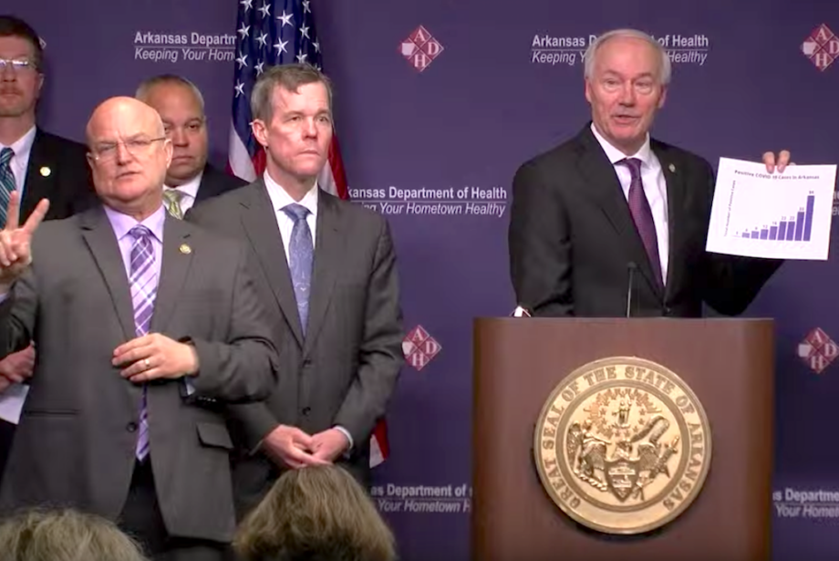 Gov. Asa Hutchinson holds a chart showing the rise of confirmed cases of the coronavirus in Arkansas.