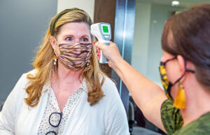 Office etiquette has expanded to embrace temperature checks as part of the COVID-modified reception routine. Kim Battle, director of property management at the Little Rock office of Colliers International, undergoes a Fahrenheit scan by Leslie Wilson, human resources director with Colliers.