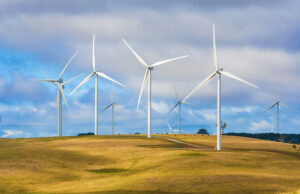 Group of wind turbines at a wind farm on a hill with cattle grazing beneath, creating renewable energy in Taralga NSW Australia.