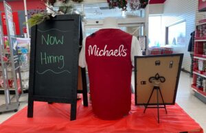 Maple Grove, Minnesota - November 14, 2021: Now Hiring sign inside of a Michaels store - retail stores are in desperate need of workers and help for the holidays