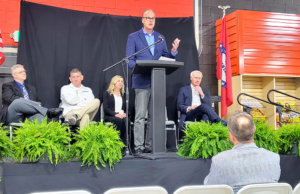 The Toro Company Chairman and Founder Rick Olson, behind the podium, speaks at an event in Batesville on April 21 celebrating the company's acquisition of Intimidator Group. Behind him, in a white shirt, is Intimidator Group founder Robert Foster.