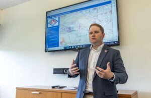 A man in a suit stands in front of a screen displaying a map