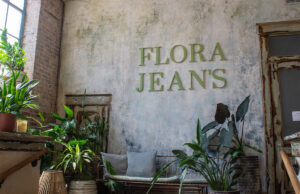 A concrete wall with plants and Flora Jeans in green font