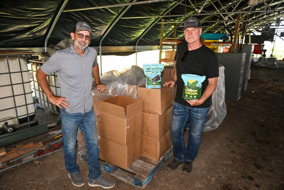 Jody Hardin and Richard Ims, CEO and chief business officer at Carbon Chicken Project LLC, stand with their 4-pound bag of fertilizer at the company’s 11-acre innovation farm in Fayetteville. [Michael Woods]
