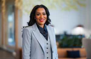 Latriece Watkins, African American woman in a gray suit in front of a blurred office background.