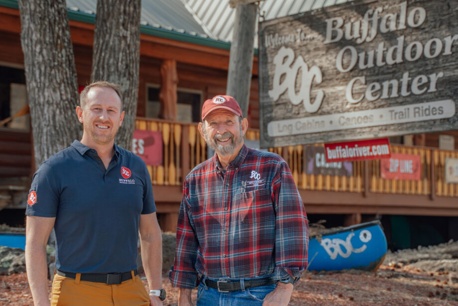 Austin Albers standing to the left of Mike Mills in front of the Buffalo Outdoor Center, a log-cabin structure retail space.