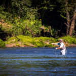 A man wearing waders, fly-fishing in a river.