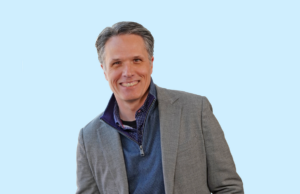 Chris East, Principal Architect at Cromwell Architects Engineers of Little Rock. A middle-aged man in a gray blazer and blue shirt on a light blue background.