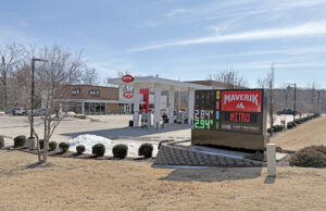 A Maverik gas station, displaying a digital sign with gas prices and a row of gas pumps and the store, a blocky brown and white building.