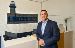 Lance Belline, an older white man, wearing a suit with no tie, standing in front of the reception desk at Lighthouse Financial.