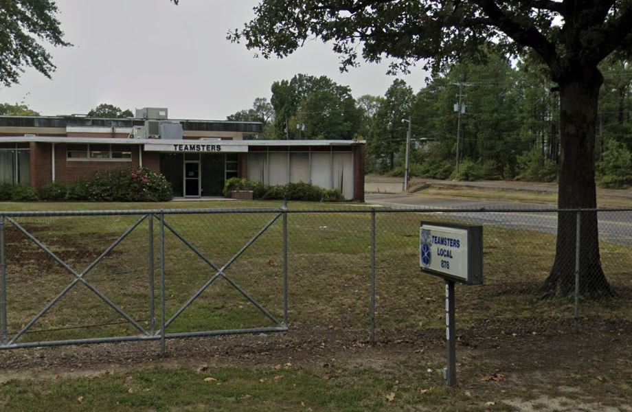 A streetview of the Teamsters Local 878 building in Little Rock, a single story brick building with tall windows behind a chain-linked fence.