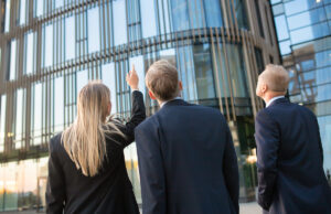 Three business people examining a high-rise building from the street.