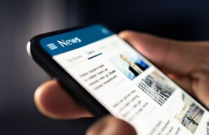 A very close up image of a person holding a phone, there is a generic news page on the phone.