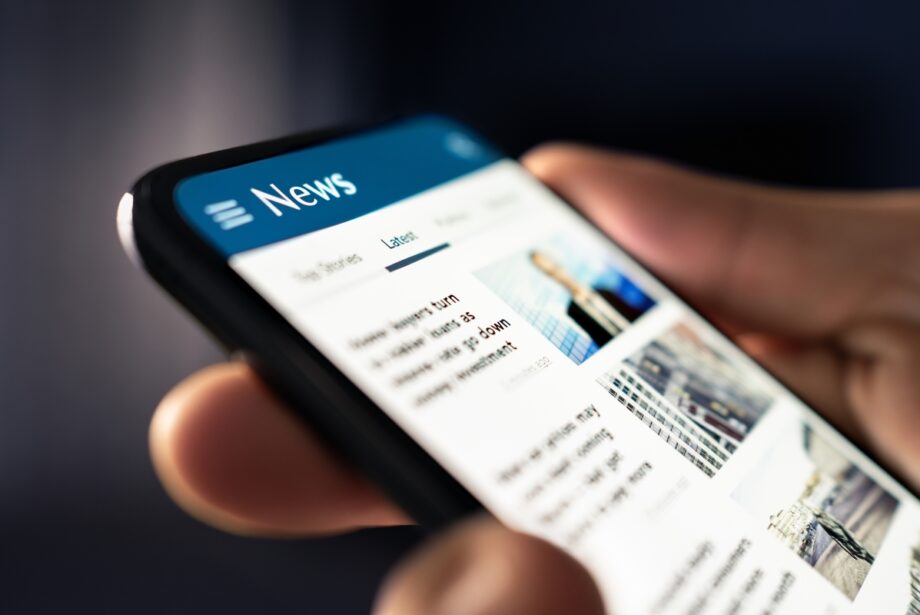 A very close up image of a person holding a phone, there is a generic news page on the phone.