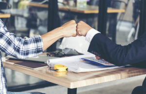 A construction worker and a man in a business suit are fist bumping.