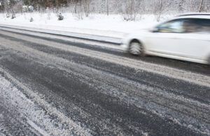 A snapshot of a car zooming past on an icy, semi-plowed road.