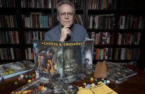 A man sits behind a tabletop RPG board with fantasy accessories on the table in front of him