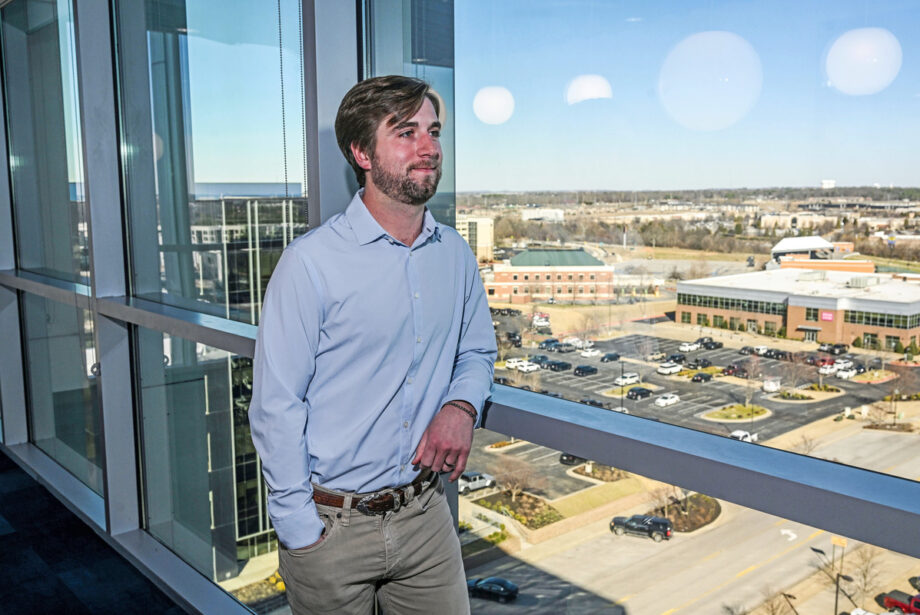 Johnny Galloway, a younger white man in a crisp button-down and khakis standing next to tall windows looking out over a parking lot.