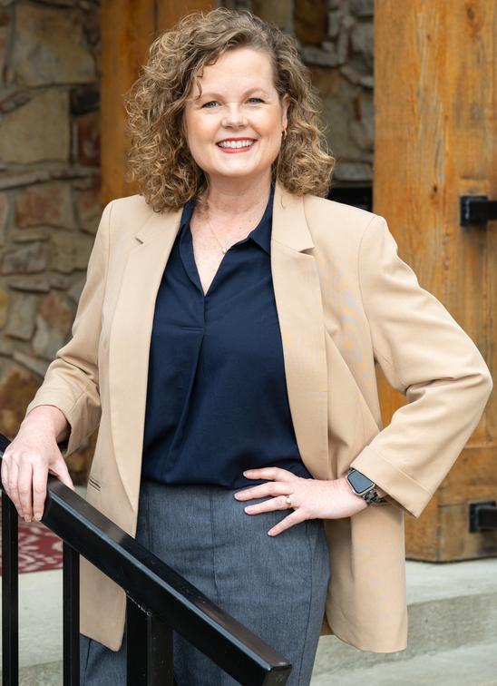 Gail Murdoch, a middle-aged white woman with curly hair in a navy blouse, gray slacks and a tan jacket standing outside a building.