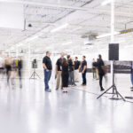 People stand in a wide open white room in a manufacturing facility