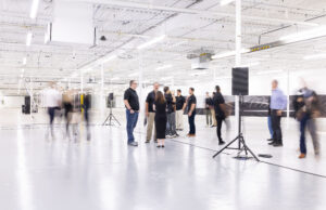People stand in a wide open white room in a manufacturing facility