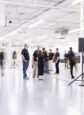 People stand in a wide open white room in a manufacturing facility