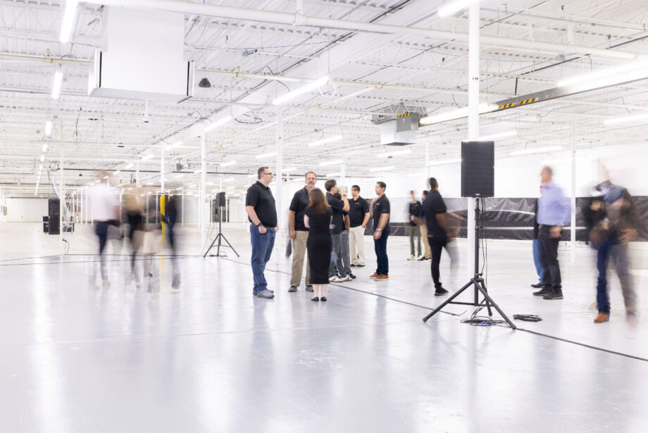People stand in a wide open white room in a manufacturing facility